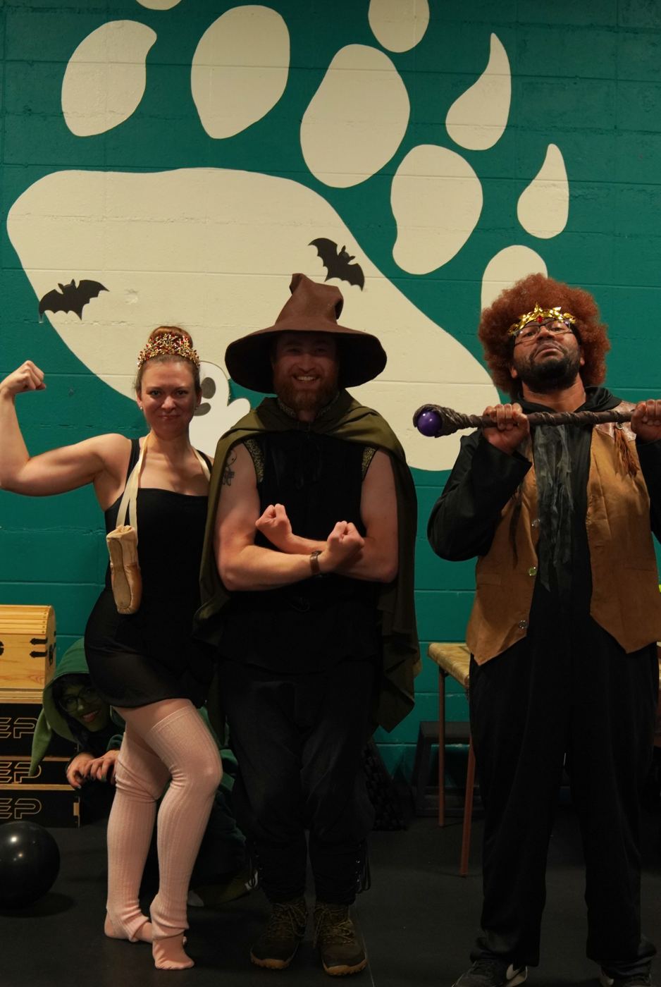 Halloween costume winners flexing in front of the bear-paw mural at the Forge